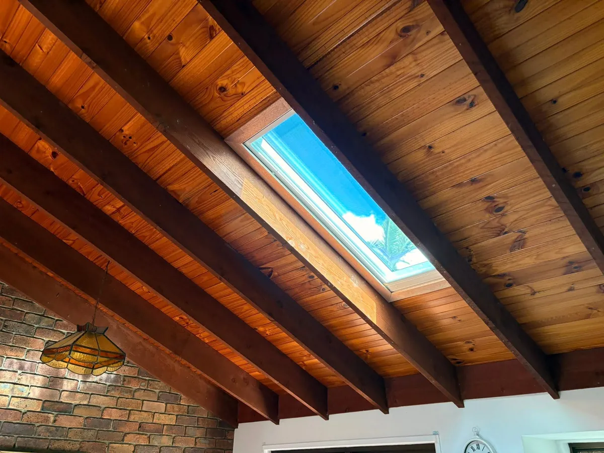 Roof window set between dark timber beams in a raked ceiling