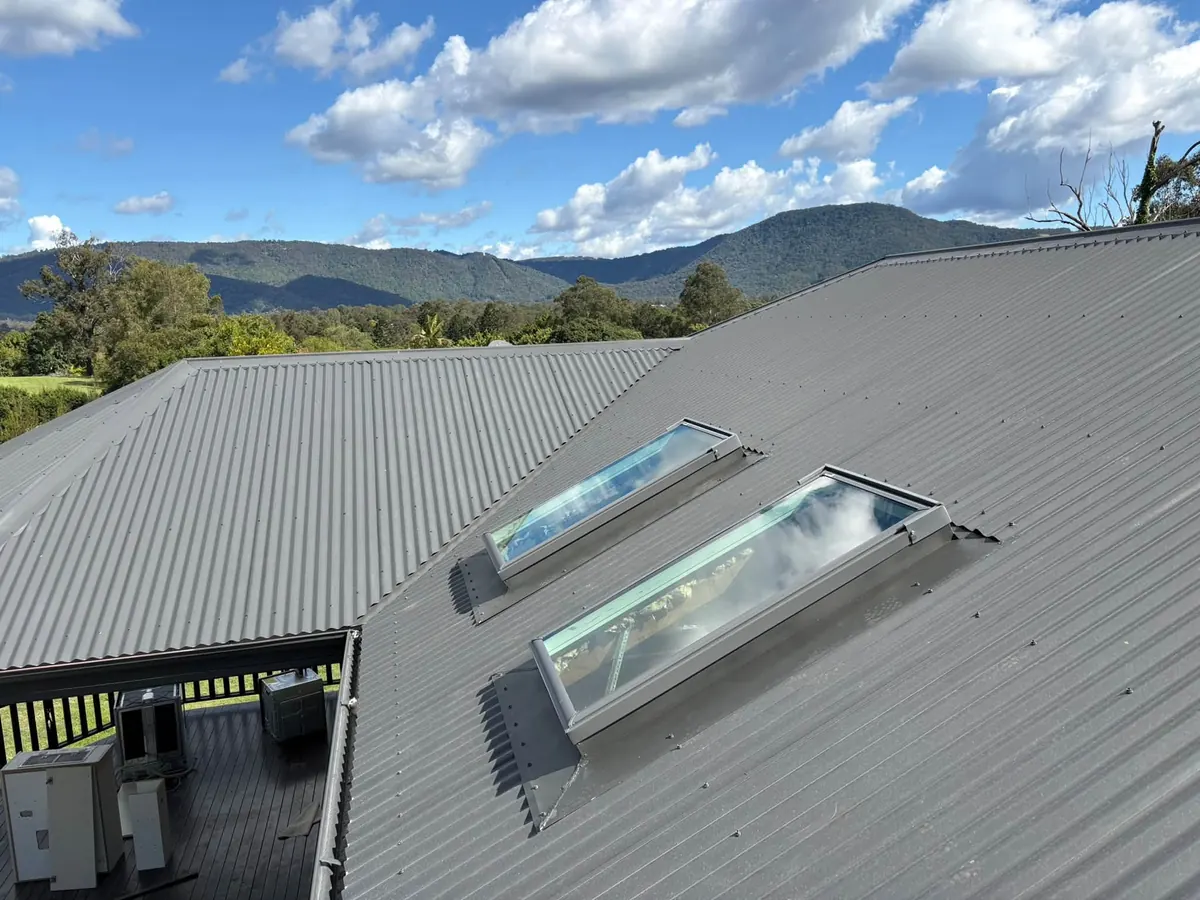 Two roof windows on a grey metal roof with a mountain view